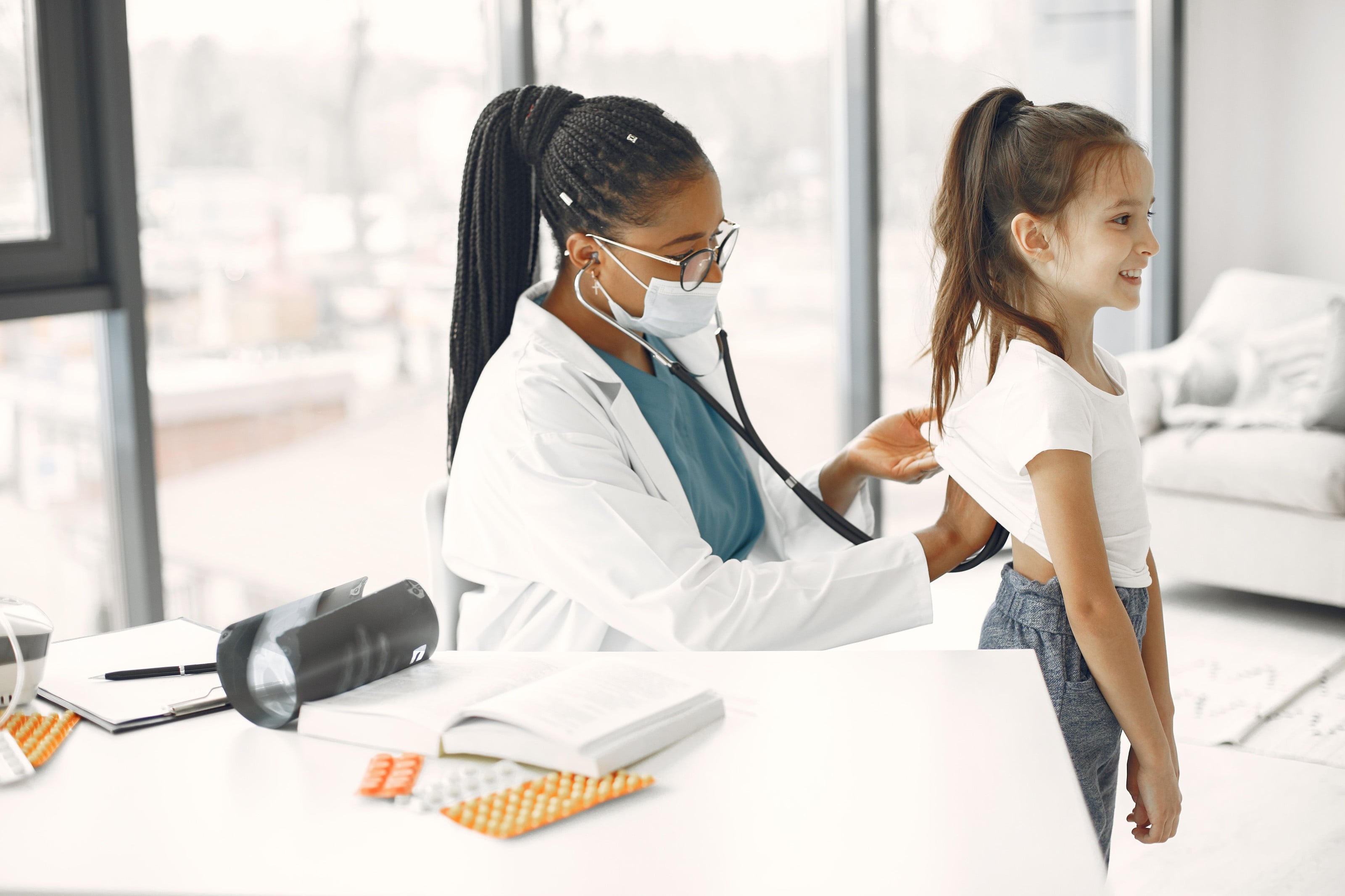 Médica auscultando la espalda de una niña en el consultorio