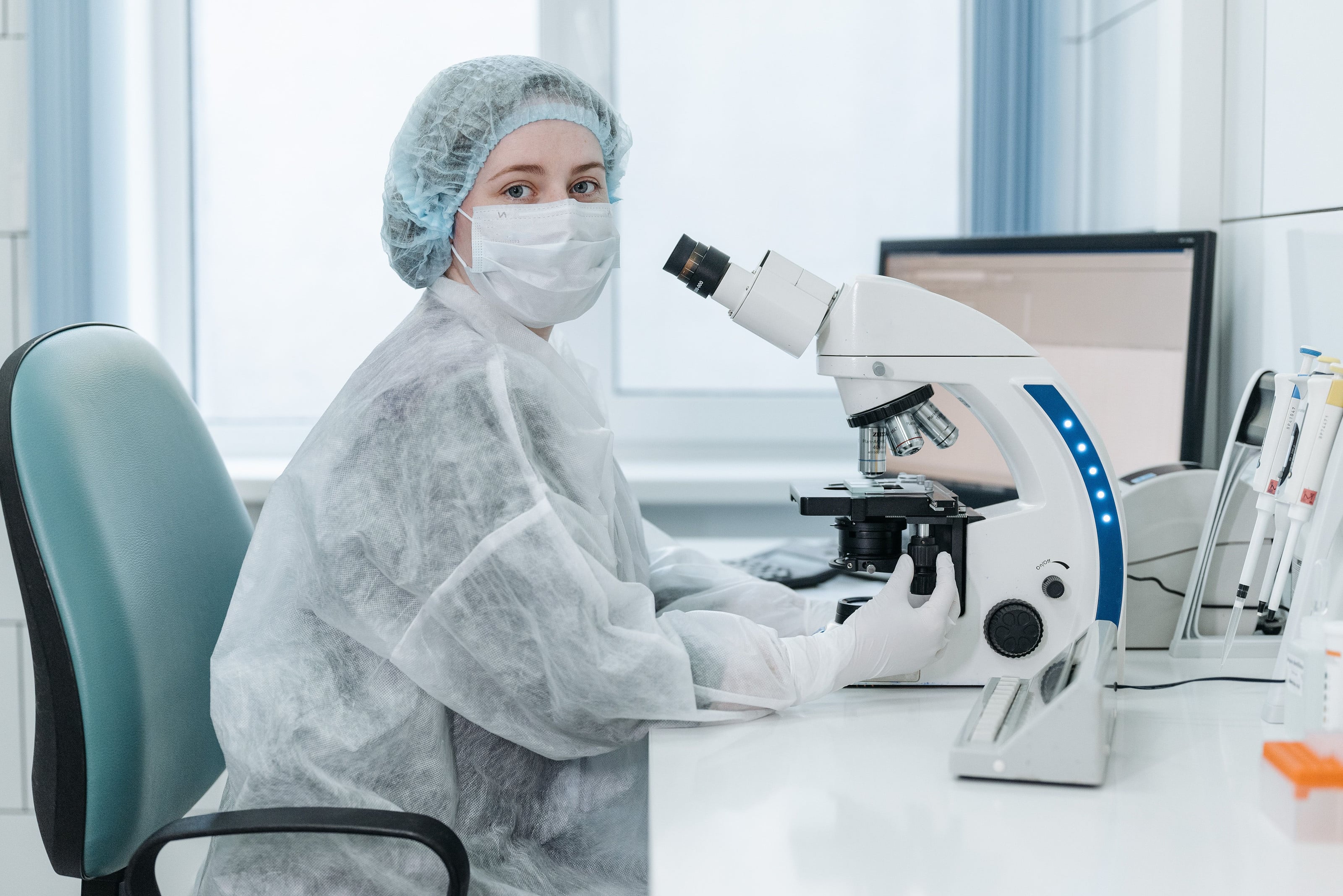 Bacterióloga con tapabocas junto al microscopio en el laboratorio